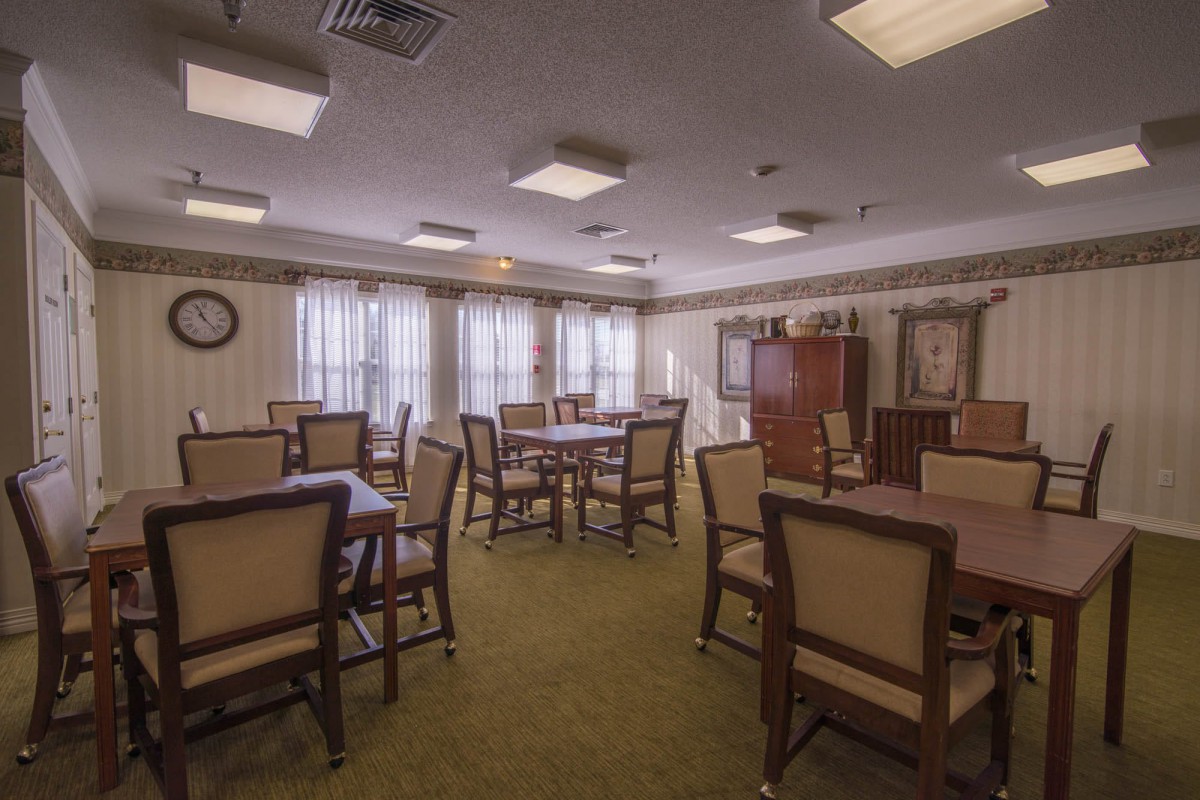 A cozy dining room with multiple tables and chairs, well-lit by overhead lights and natural window light.