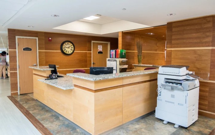 A modern reception area featuring a wooden desk, office equipment, and a wall clock.