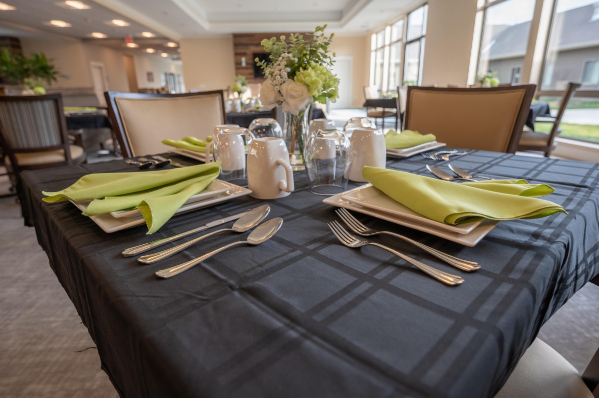 An elegantly set dining table with green napkins and fine cutlery, ready for guests in a restaurant setting.