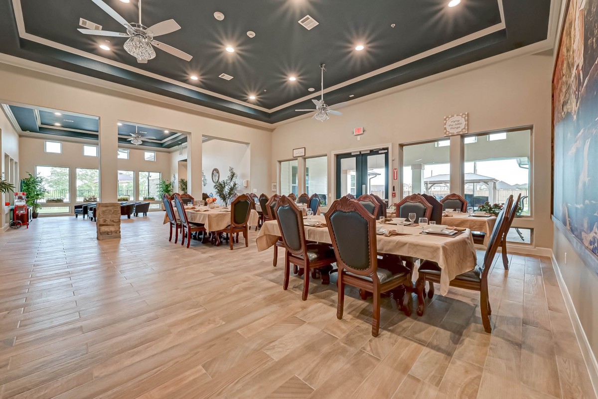 A spacious dining room with elegantly set tables and chairs, ceiling fans, and large windows providing natural light.