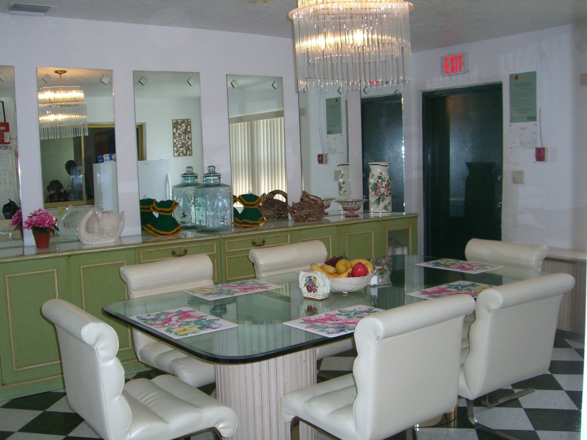 A stylish dining room featuring a glass-top table, cushioned chairs, and an elegant chandelier.