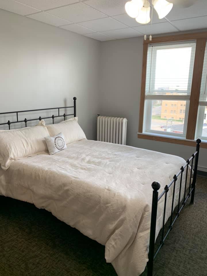 A cozy bedroom with a neatly made bed, brightened by natural light from a large window.