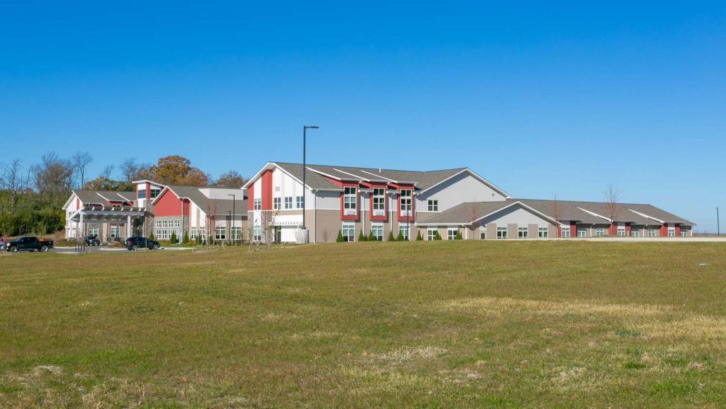 A modern residential building set against a clear blue sky with an open grassy field in the foreground.