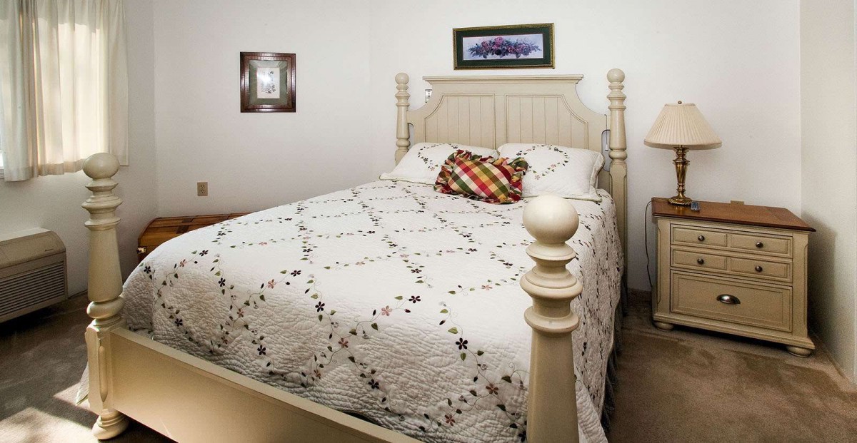 A cozy bedroom with a neatly made bed featuring a patterned quilt and decorative pillows.