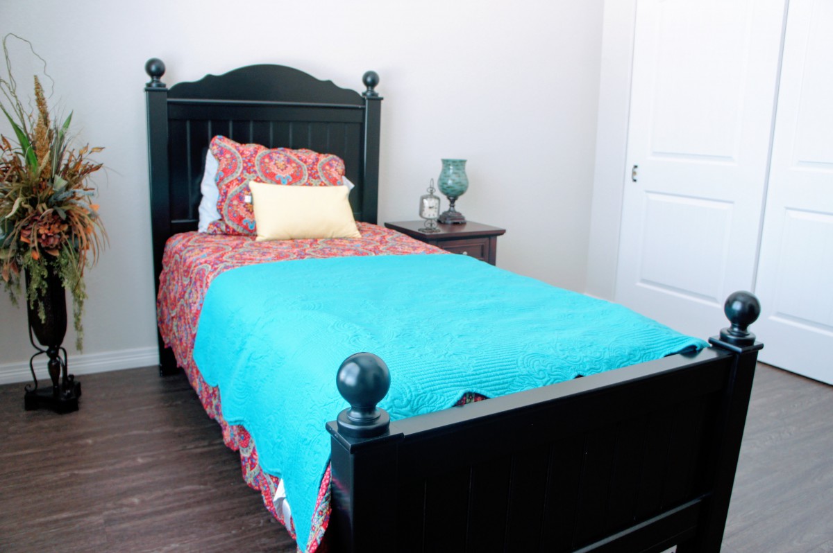 A cozy bedroom with a single bed featuring a turquoise blanket and decorative pillows.
