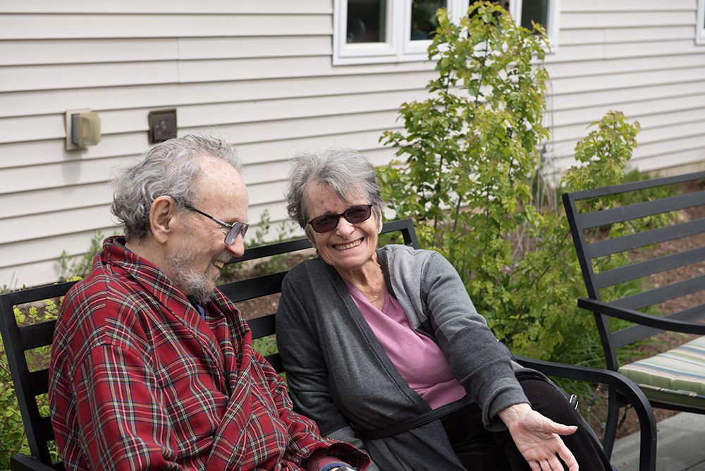 An elderly couple sitting together and smiling in a garden setting.