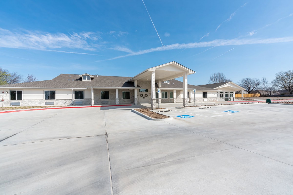 A modern building with a prominent entrance and an adjacent parking lot under a clear blue sky.