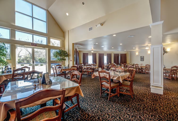 A spacious dining area with neatly arranged tables and chairs, featuring large windows that let in natural light.