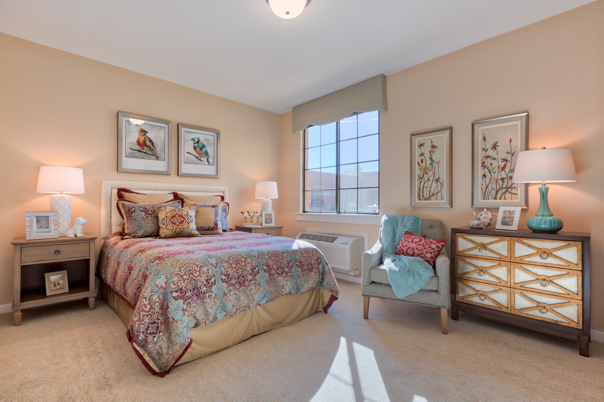 A well-decorated bedroom featuring a cozy bed, armchair, and large window allowing natural light to fill the space.