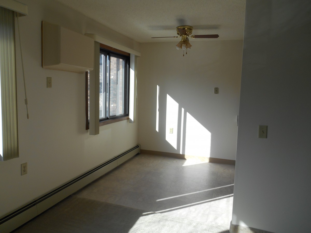 An empty room with sunlight streaming through the window, featuring a ceiling fan.
