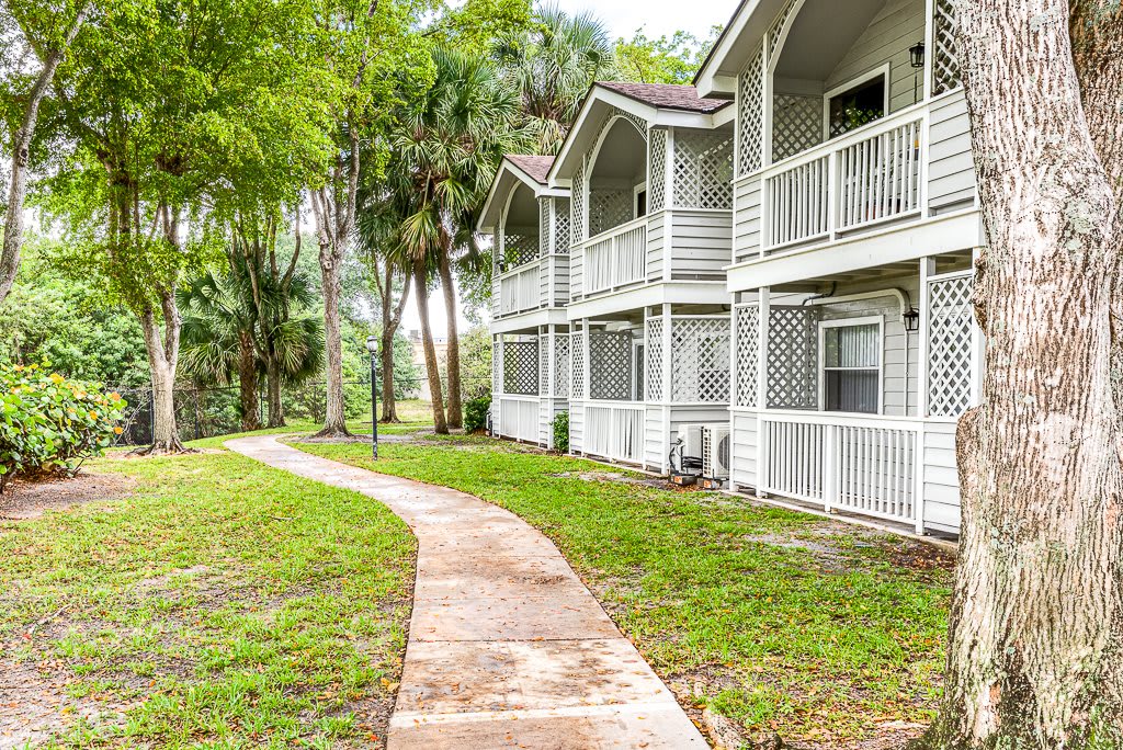 A scenic view of a residential building with a winding pathway surrounded by lush greenery and trees.