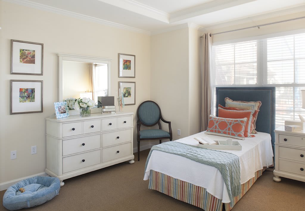 A neatly arranged bedroom with a single bed, dresser, and chair near a window.
