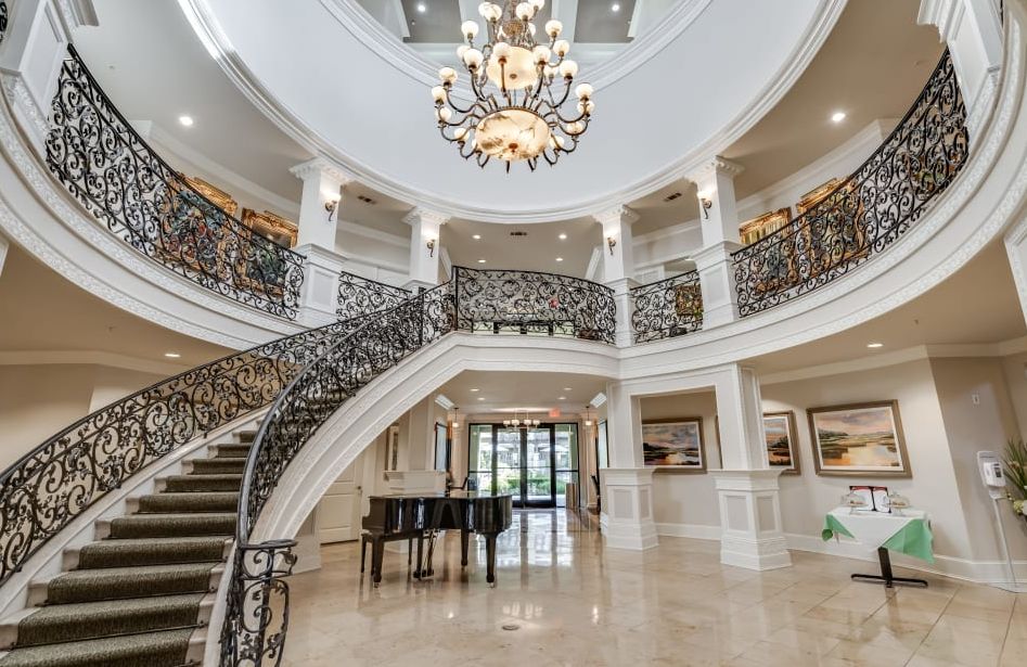 A luxurious interior featuring a grand staircase with ornate railings and a central chandelier, complemented by a sleek piano.