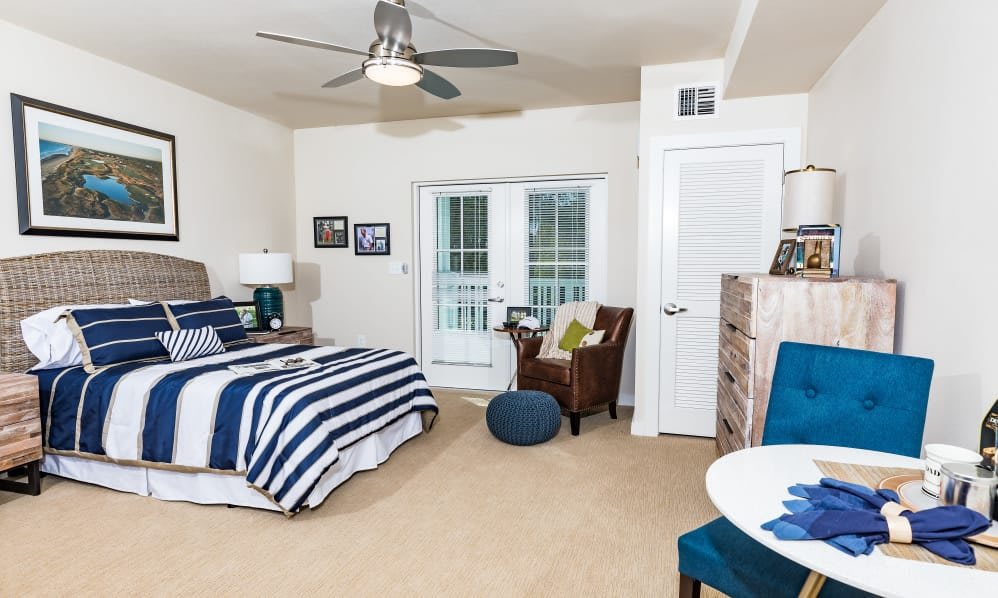 A modern bedroom with striped bedding, an armchair, and balcony access.