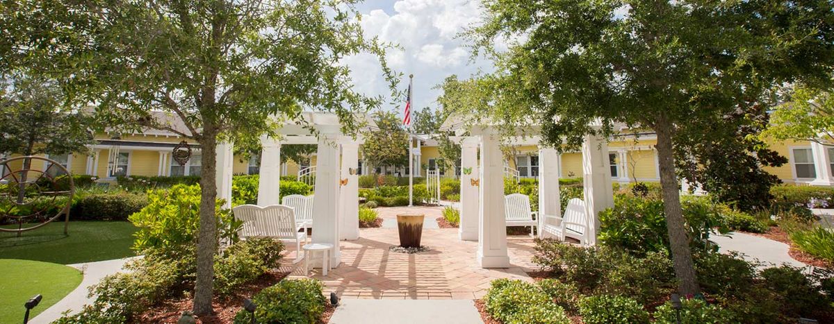 A beautiful garden featuring a pergola with benches, surrounded by lush greenery and centered around a flagpole.