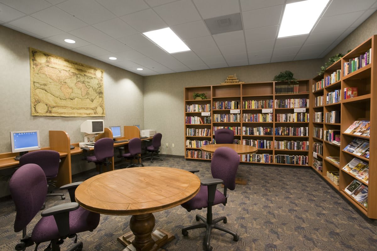 A cozy library space with bookshelves, tables, chairs, and computers for study and research.