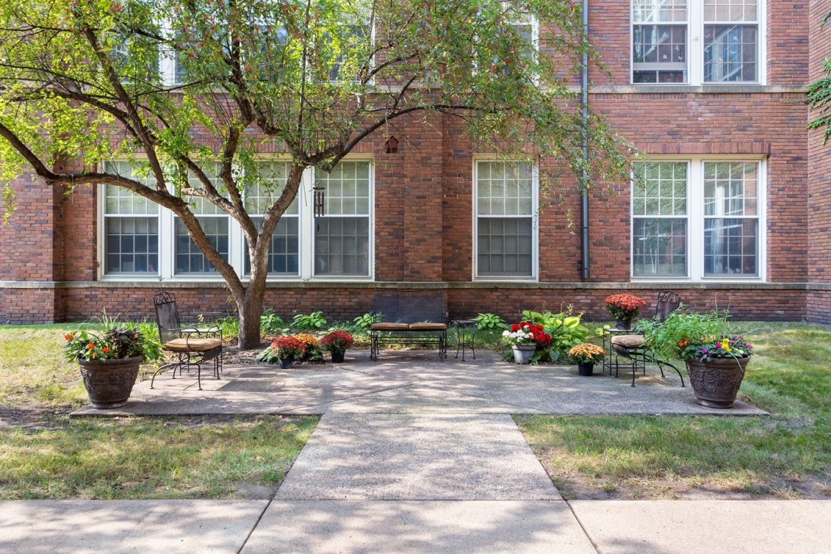 A serene garden area with benches, flowers, and trees in front of a brick building.
