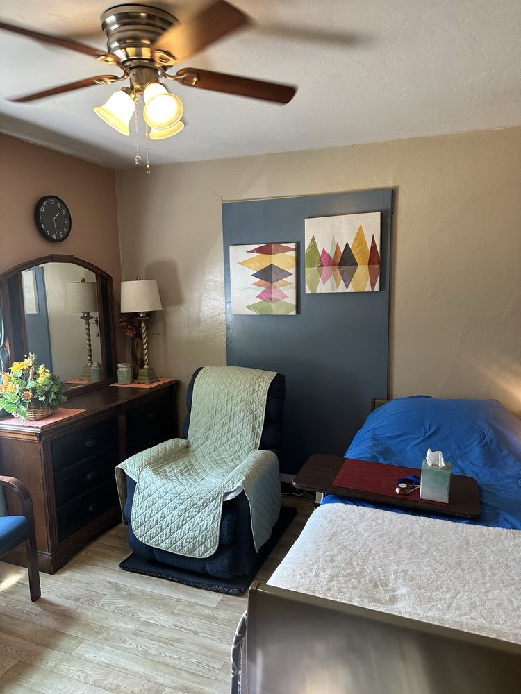 A cozy bedroom with a comfortable chair, a dresser with a mirror, and colorful artwork on the wall.
