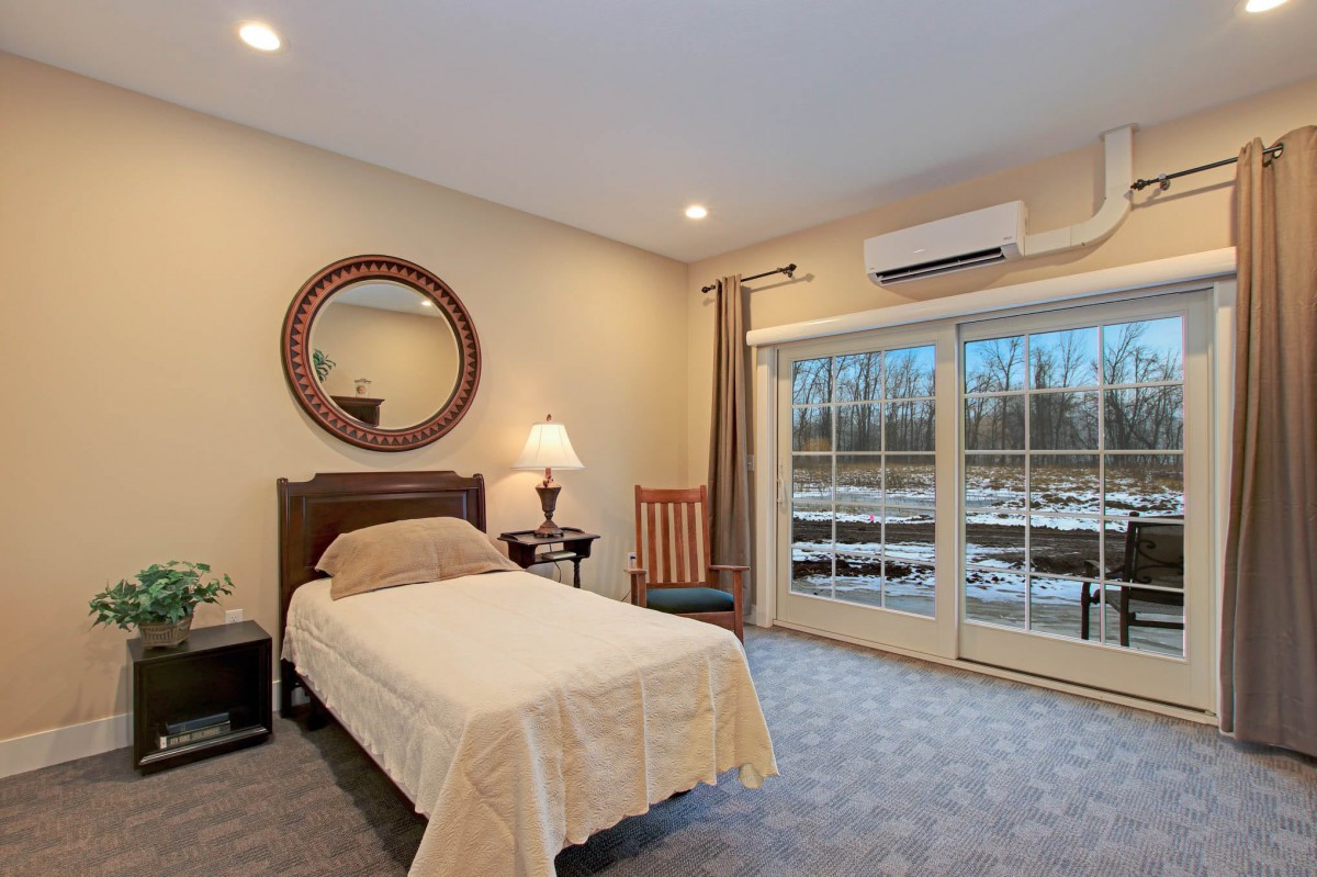 A cozy bedroom with a single bed, decorative mirror, and glass doors leading outside.
