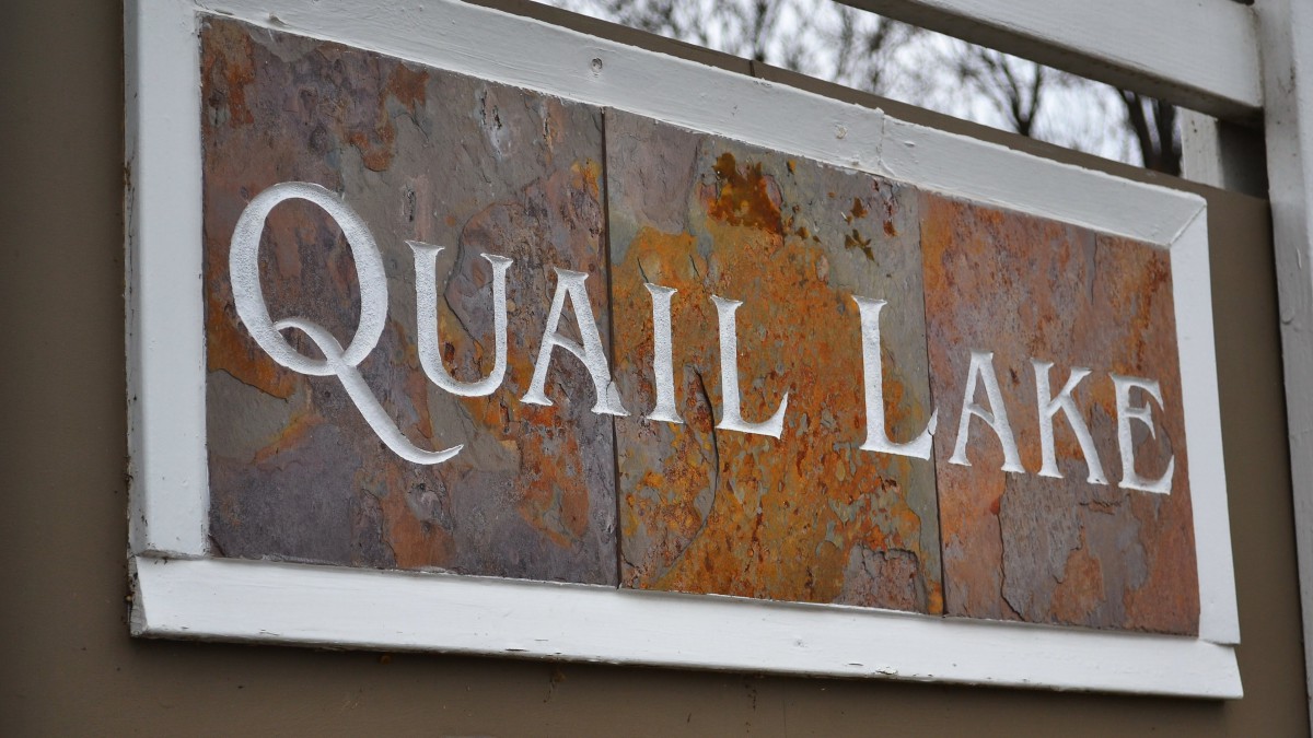 A rustic sign displaying the text 'QUAIL LANE'.