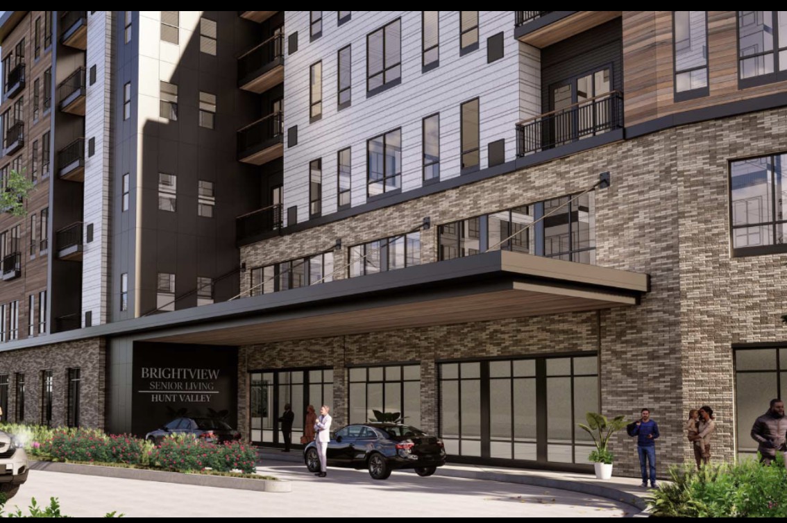 A modern hotel entrance with a stone facade, featuring people and a car in front.