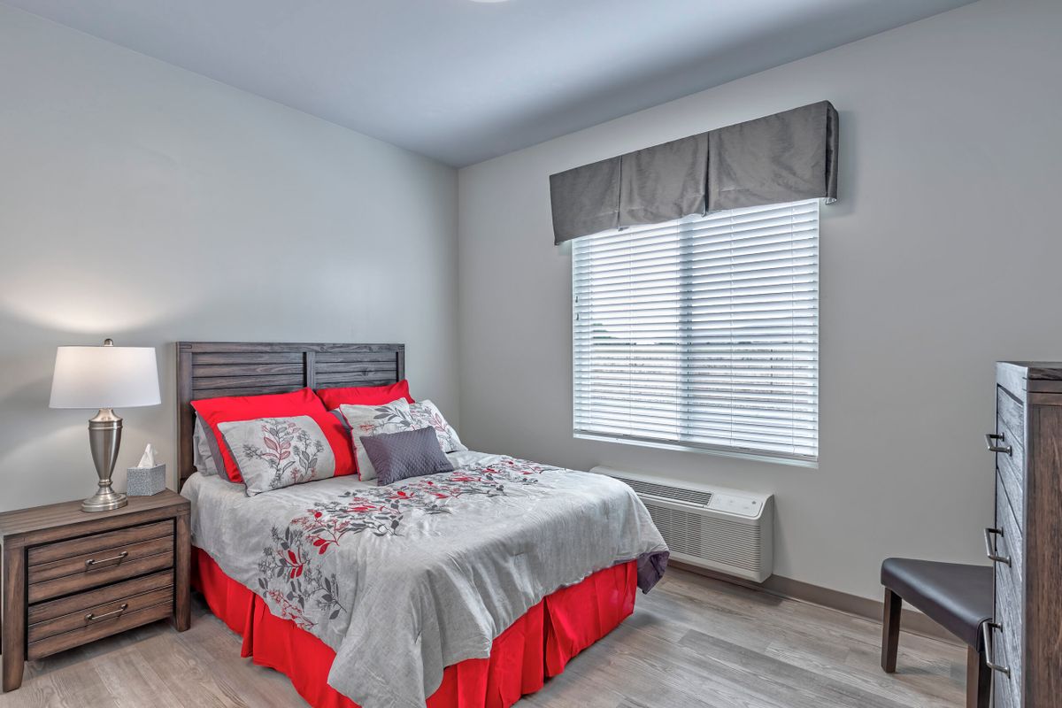 A modern bedroom with red-accented bedding and a large window.