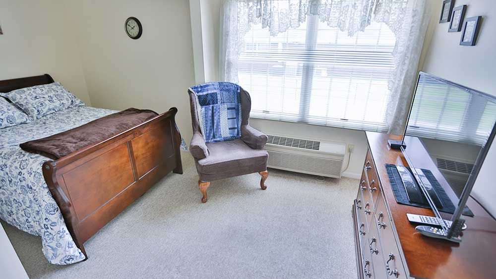 A cozy bedroom corner with a chair and dresser near a sunlit window.