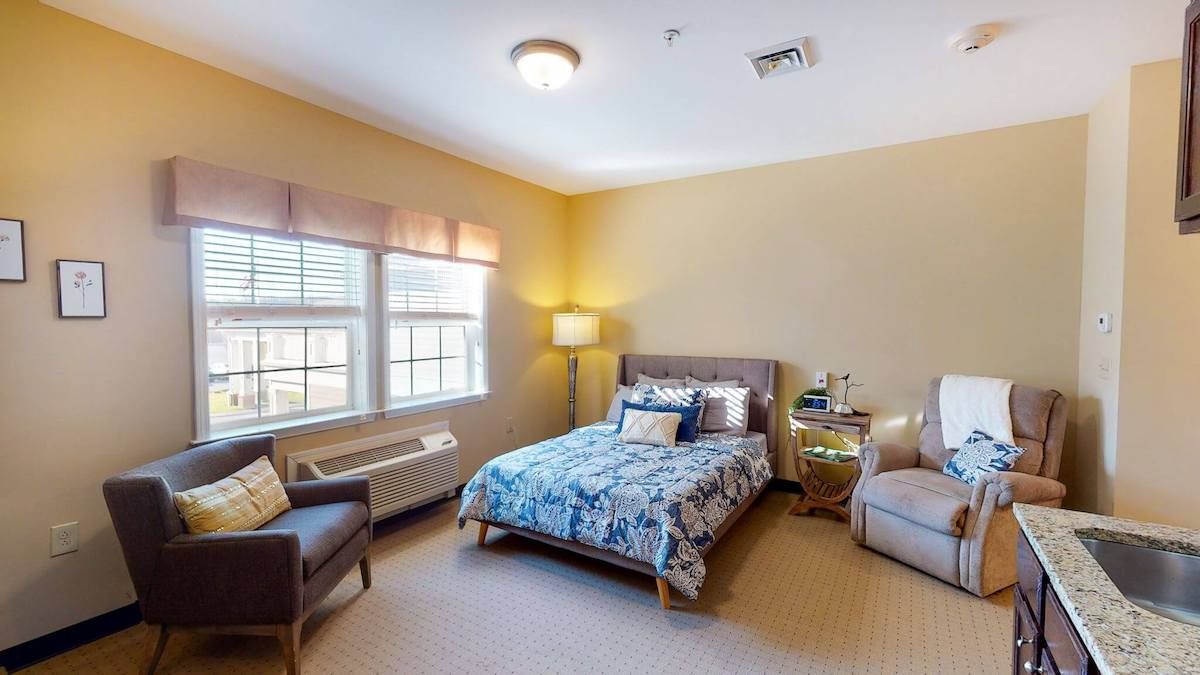 A cozy bedroom with a neatly made bed, comfortable seating, and ample natural light.