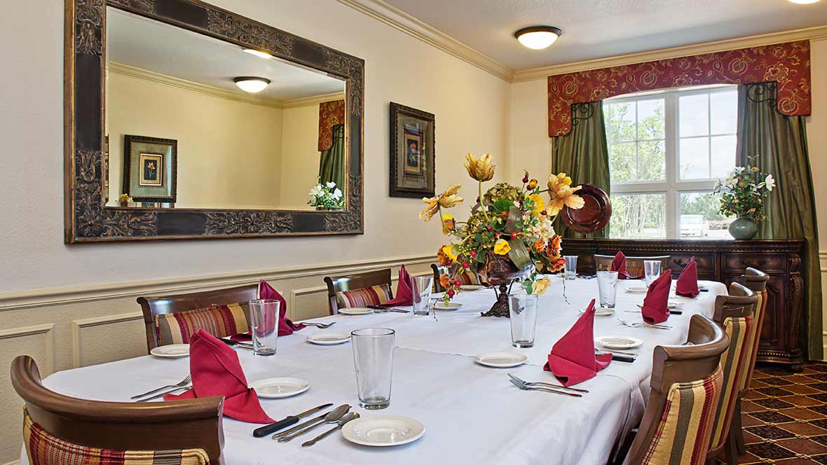 A dining room set for a meal, featuring a table with red napkins, cutlery, glasses, and a decorative flower centerpiece.