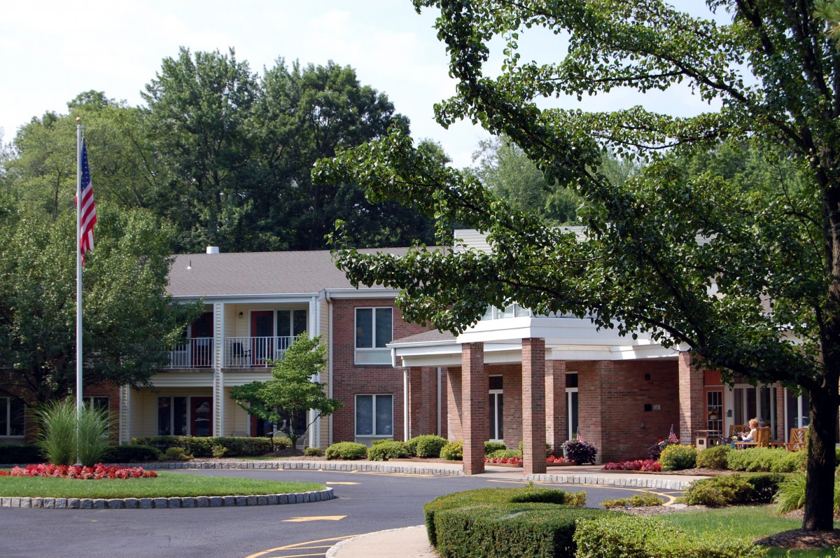 A suburban building surrounded by trees and lush landscaping, featuring a driveway.