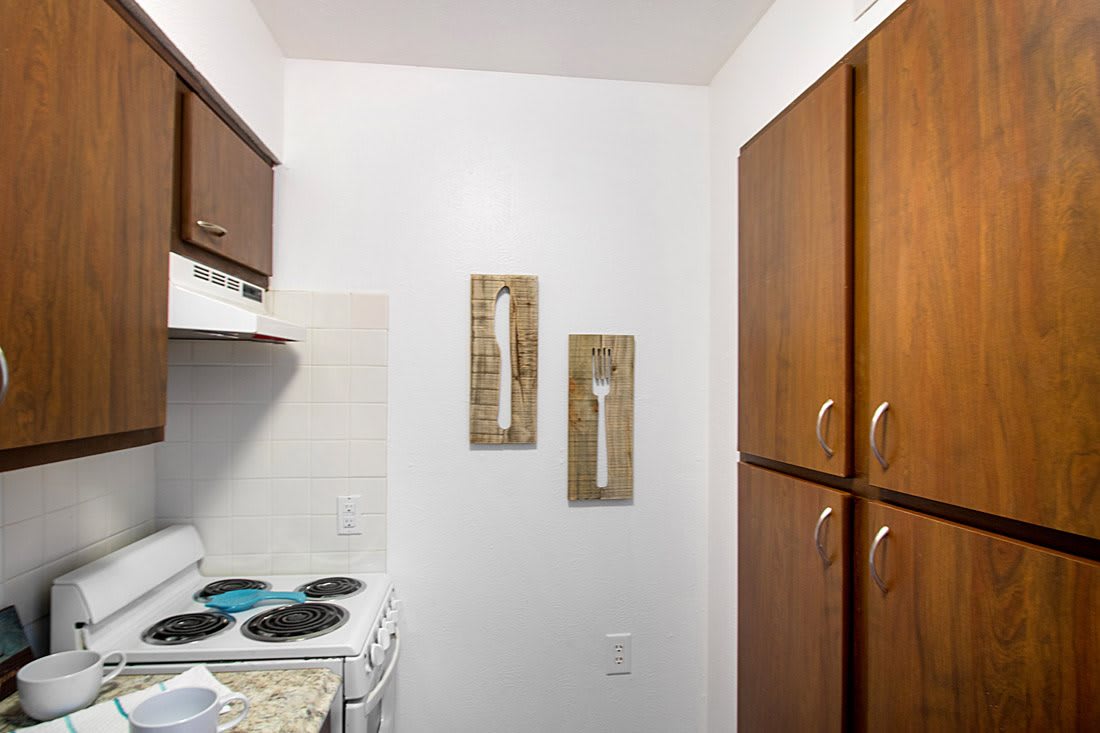 A compact kitchen with a stove and wooden cabinets, adorned with wall decor.