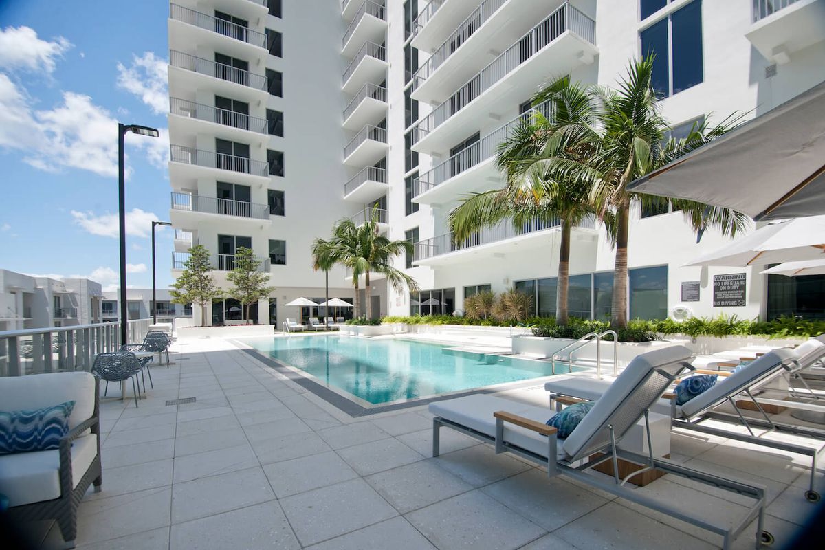 A modern residential building with a luxury outdoor pool area surrounded by palm trees.