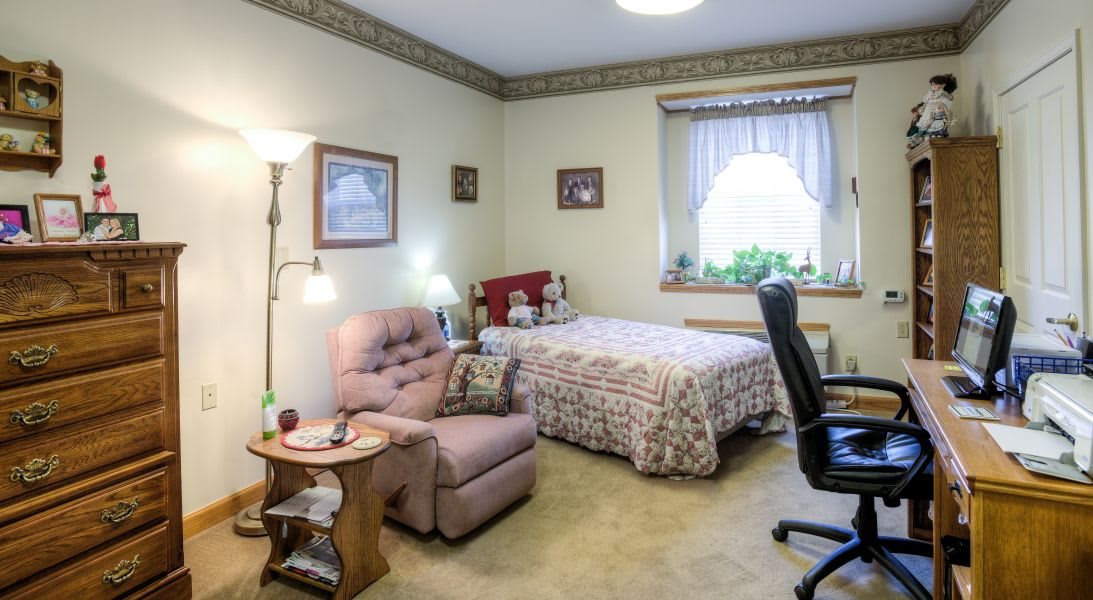 A cozy bedroom with a bed, armchair, and desk chair near a window.