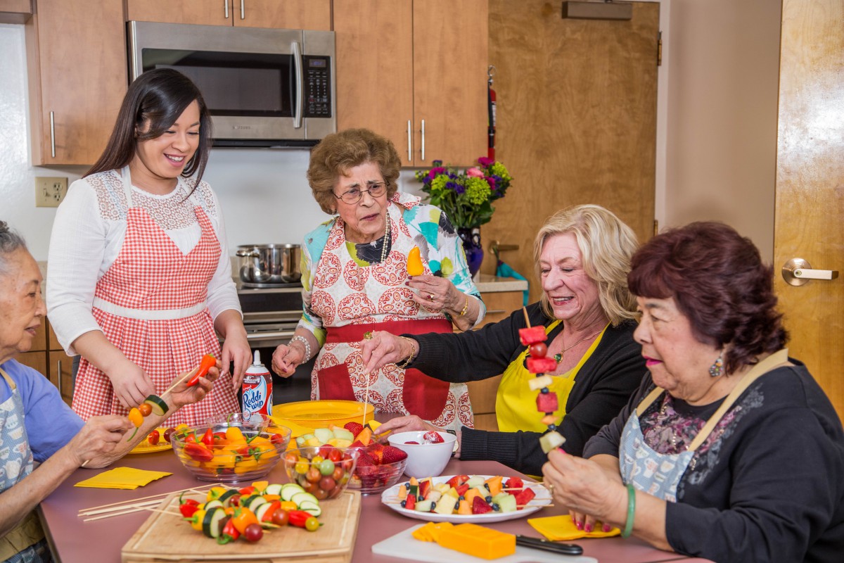 A group of women enjoying a cooking session together in the kitchen, preparing fruit skewers and sharing smiles.