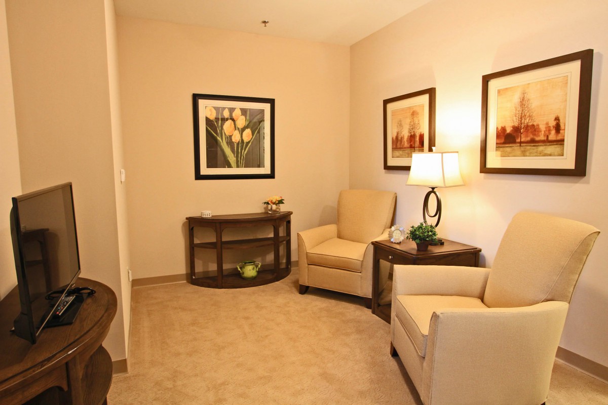 A cozy waiting room with neutral-colored armchairs, a lamp, and wall art.
