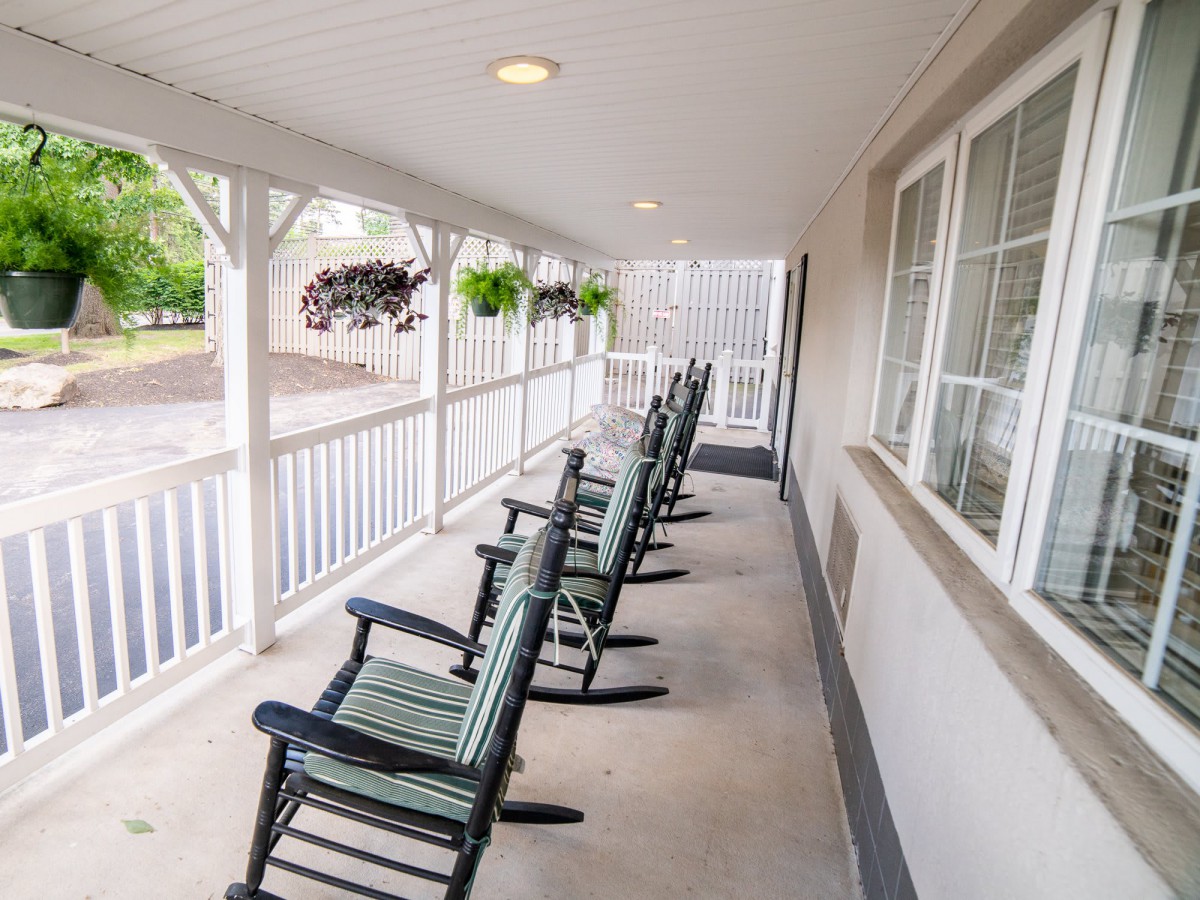 A serene covered porch with multiple rocking chairs and hanging plants.