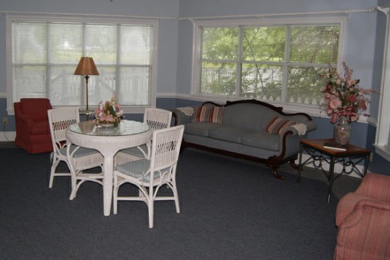 A cozy living room featuring a wicker dining set, a vintage-style sofa, and large windows allowing natural light to fill the space.