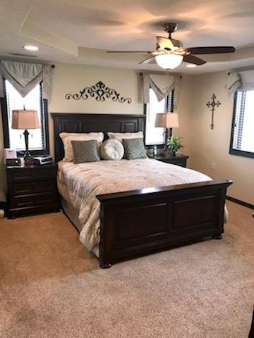 A cozy and elegantly decorated bedroom with a wooden bed frame, matching nightstands, and soft lighting from lamps and a ceiling fan.