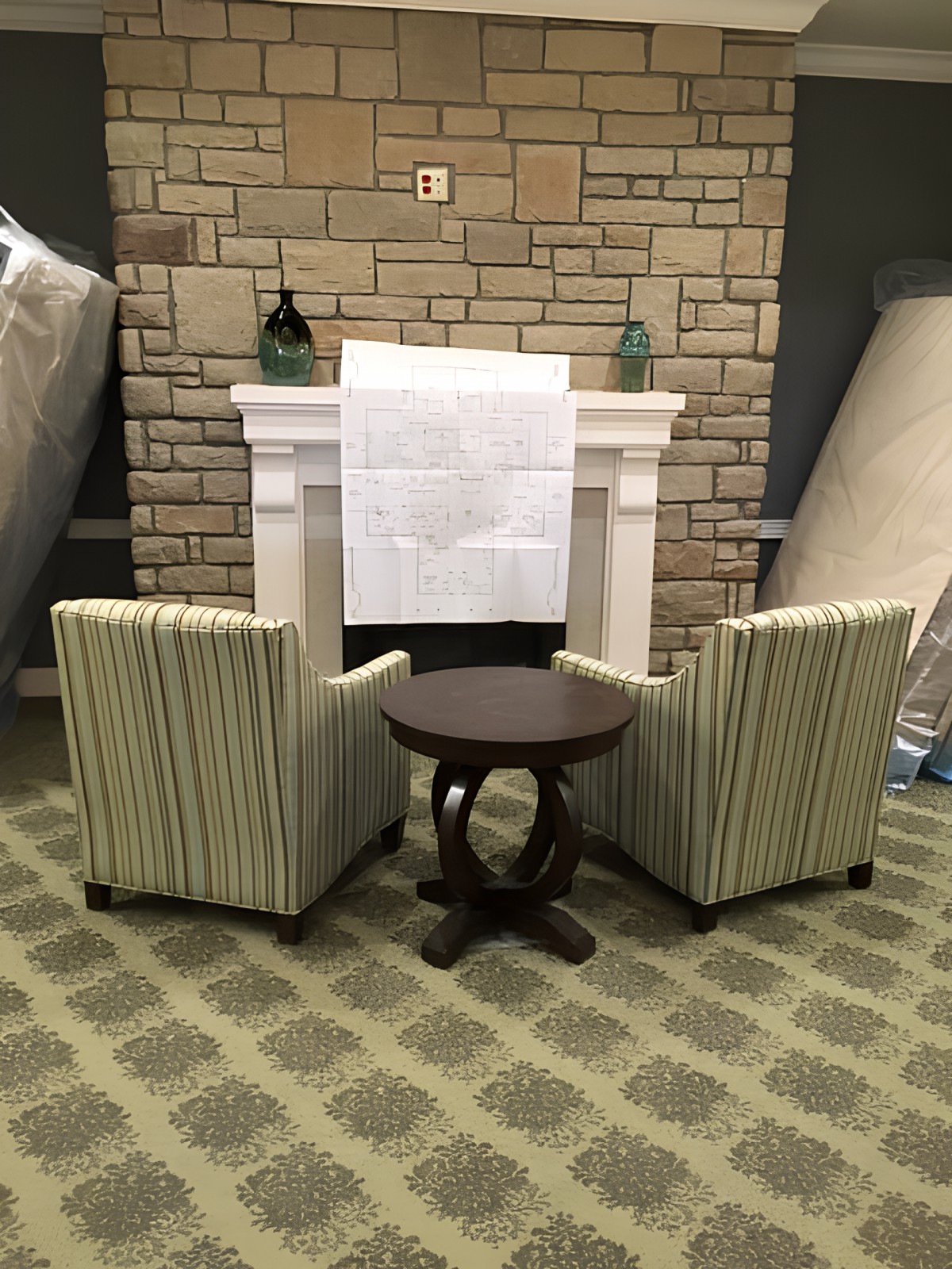 A cozy seating area with two striped chairs and a round table facing a stone fireplace.