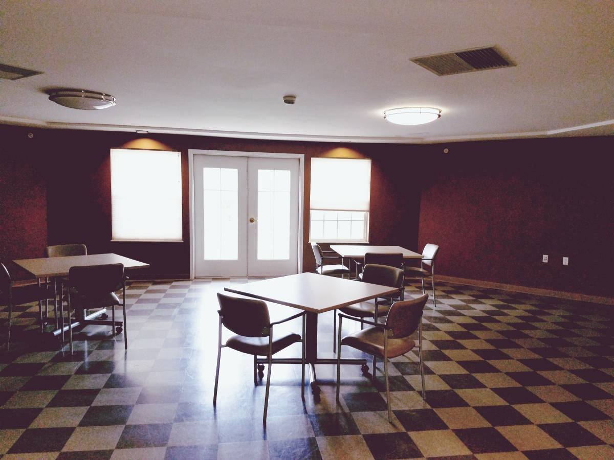 An empty room with checkered flooring, tables, and chairs.