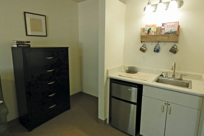 A compact kitchenette with a small fridge, sink, and storage cabinets.