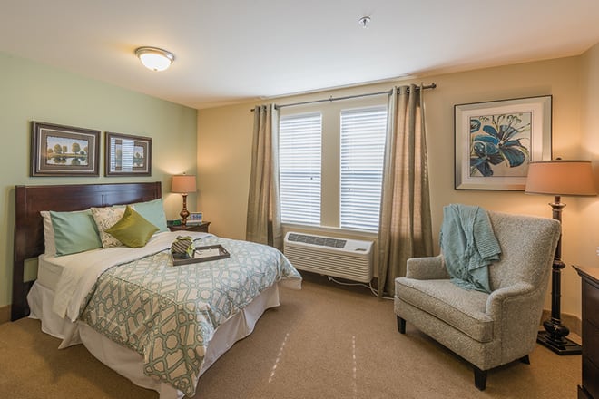 A cozy and well-decorated bedroom featuring a comfortable bed, armchair, lamp, and warm colors.