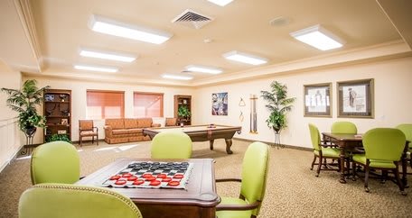 A spacious recreation room featuring a pool table, checkers game, comfortable seating, and vibrant decor.