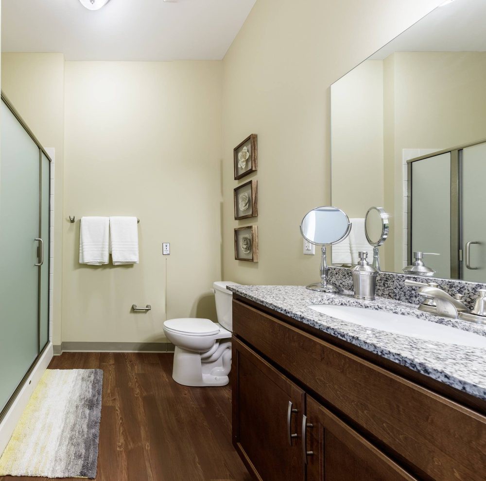 A modern bathroom interior featuring a vanity with a marble countertop, a large mirror, and a shower area.