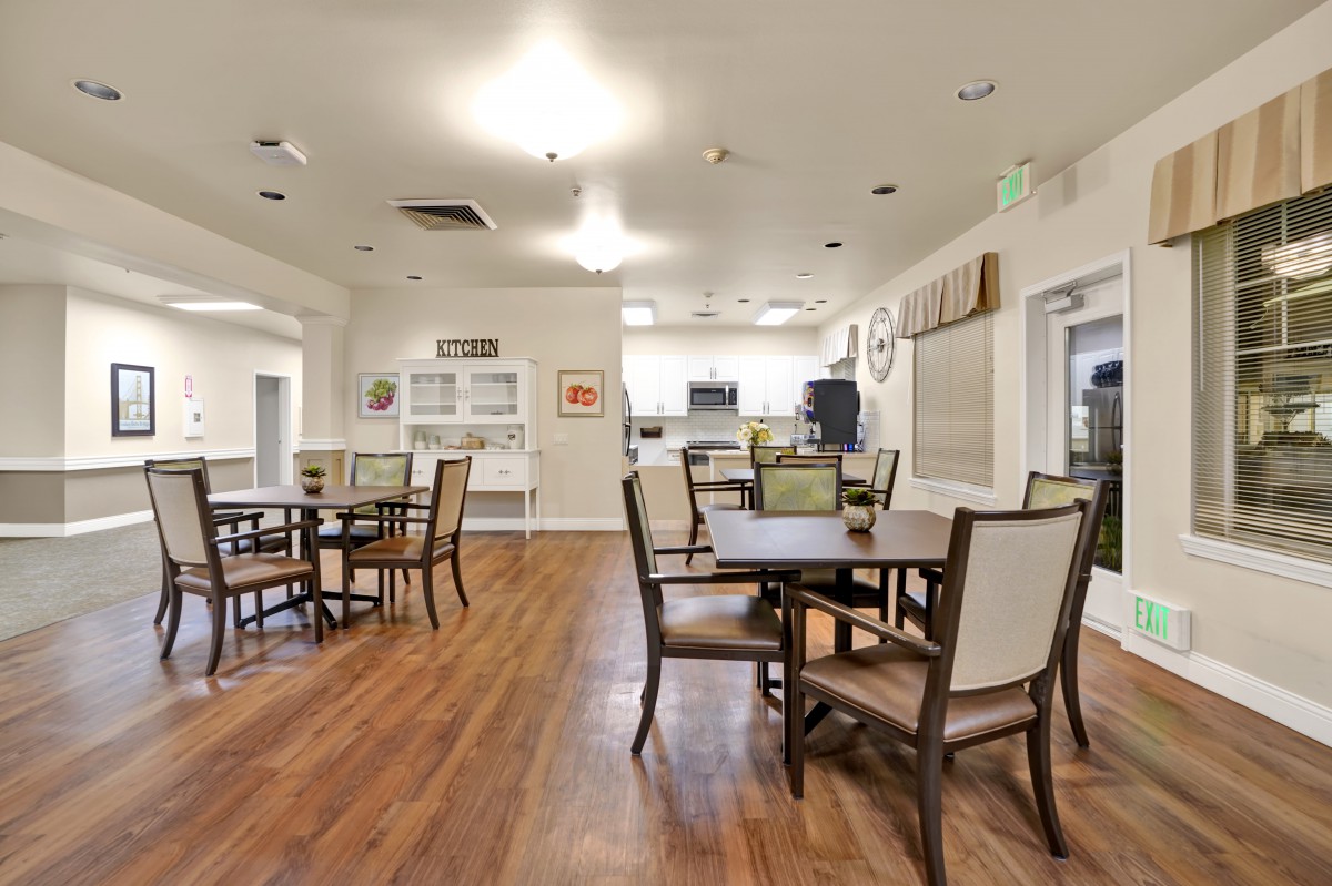 A well-lit dining area featuring wooden tables and chairs on polished wood floors.