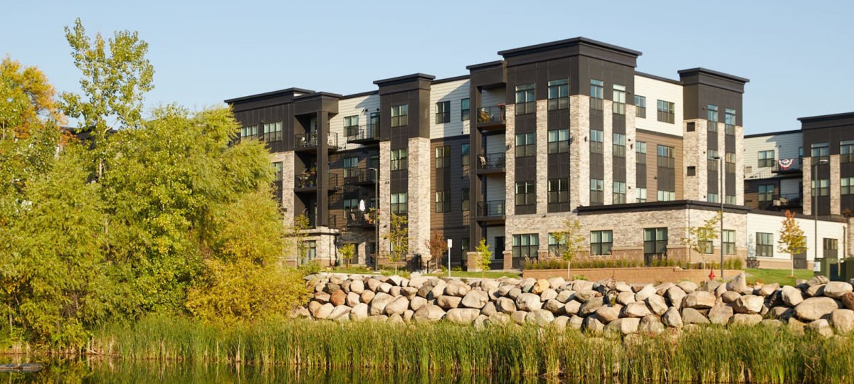 A modern apartment building with a stone facade overlooking a landscaped area.
