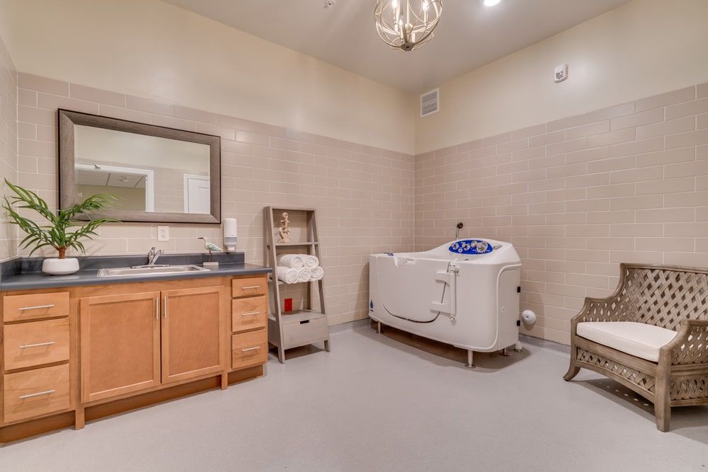 A spacious bathroom featuring a bathtub, wooden cabinets with a sink and mirror, and a towel rack under warm lighting.