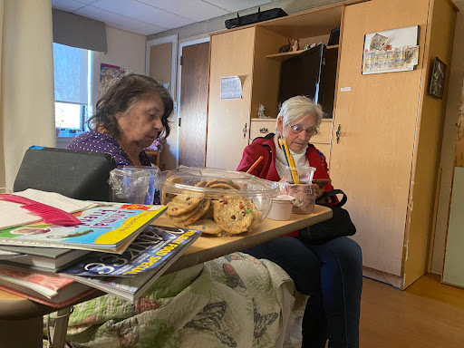 Two elderly women enjoying snacks and engaging in conversation at a care facility.
