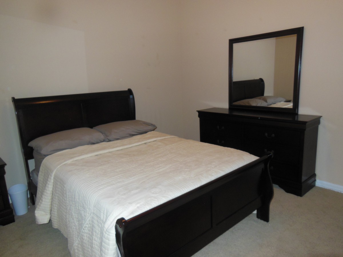 A neatly arranged bedroom featuring a bed, dresser, and mirror.