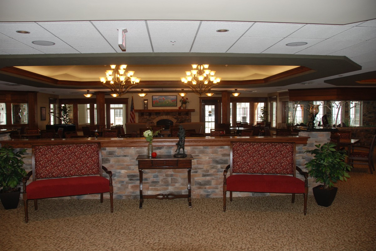 A warmly lit lobby area with symmetrical seating, chandeliers, and a central fireplace flanked by mirrors.